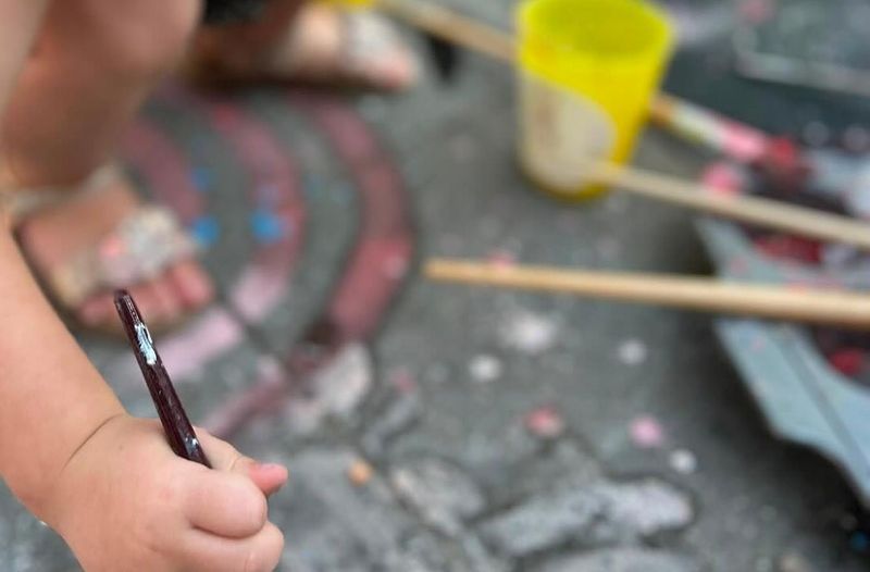 Een kinderhand met een penseel en potjes stoepkrijtverf